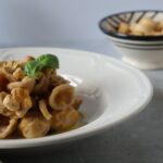 Orecchiette al grano arso con passata di pomodoro giallo, briciole di taralli e basilico, in un piatto fondo bianco