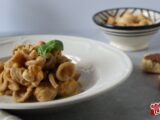 Orecchiette al grano arso con passata di pomodoro giallo, briciole di taralli e basilico, in un piatto fondo bianco