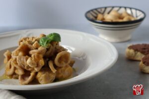 Orecchiette al grano arso con passata di pomodoro giallo, briciole di taralli e basilico, in un piatto fondo bianco
